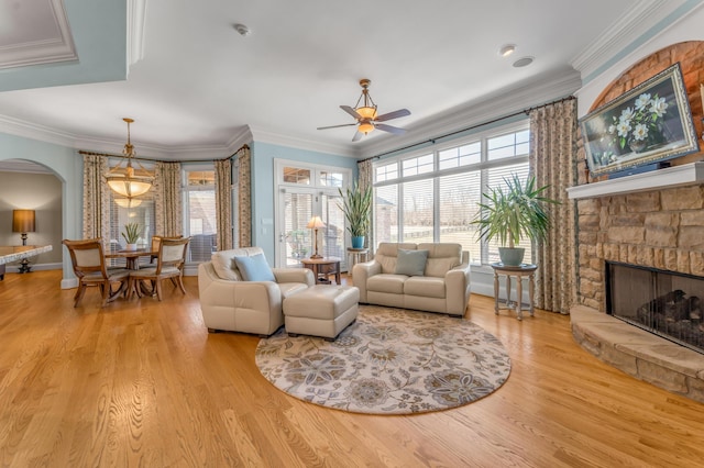 living room featuring ornamental molding, a stone fireplace, ceiling fan, and light hardwood / wood-style flooring