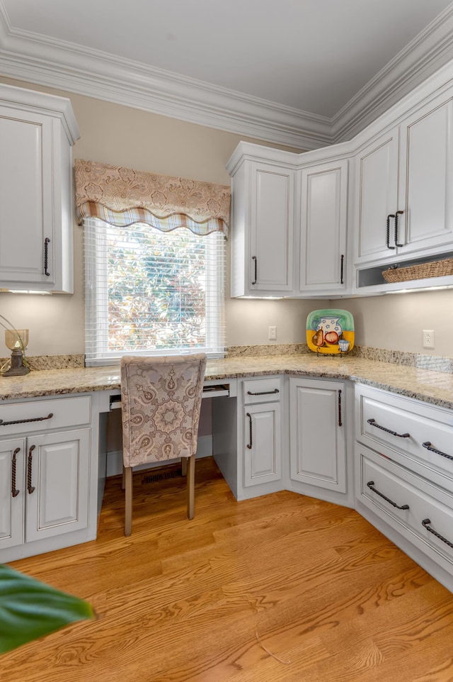 kitchen with white cabinetry, crown molding, built in desk, and light hardwood / wood-style flooring