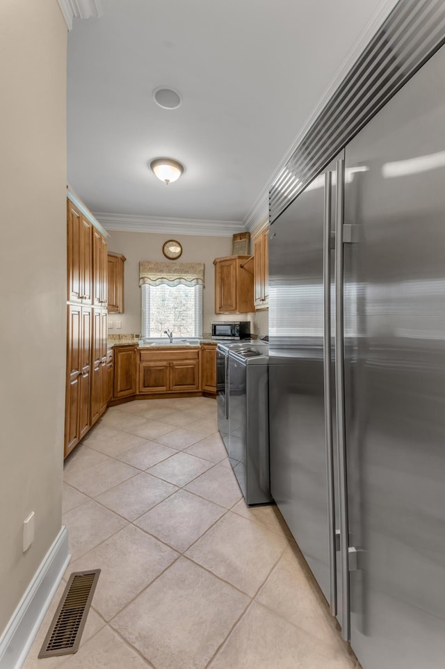 kitchen featuring appliances with stainless steel finishes, sink, light tile patterned floors, washing machine and clothes dryer, and crown molding