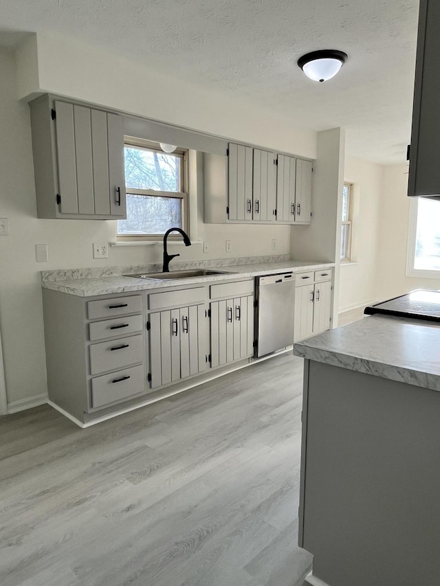 kitchen with sink, gray cabinetry, light wood-type flooring, stainless steel dishwasher, and plenty of natural light