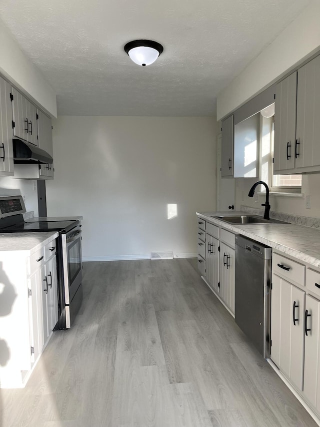 kitchen featuring sink, dishwashing machine, stainless steel range with electric stovetop, a textured ceiling, and light hardwood / wood-style flooring