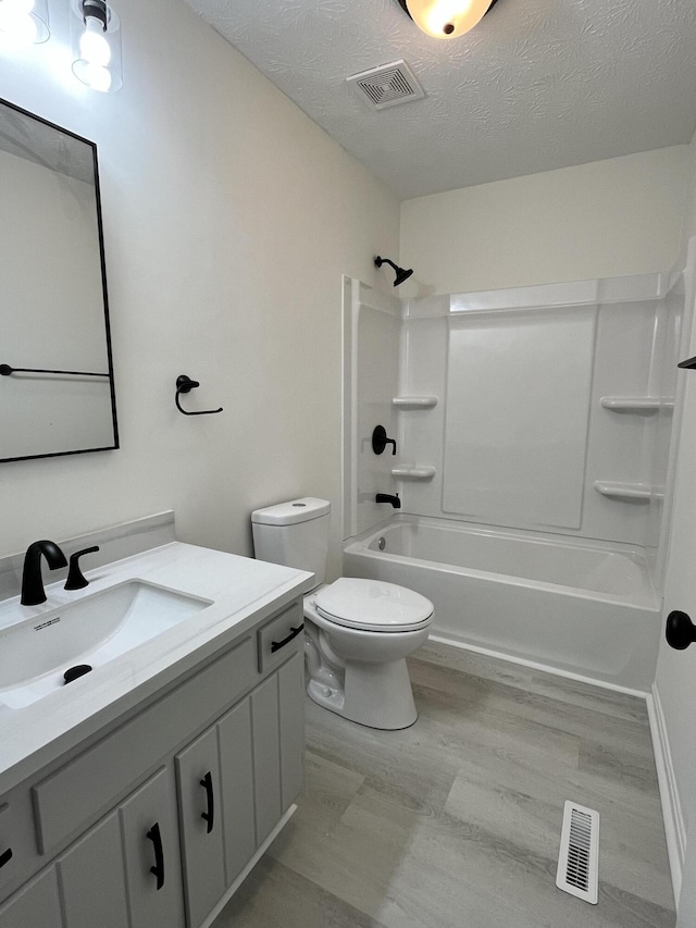 full bathroom with hardwood / wood-style flooring, vanity, toilet, a textured ceiling, and washtub / shower combination