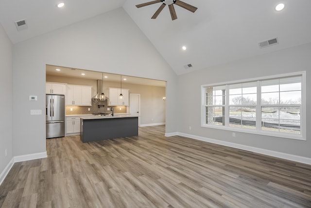 unfurnished living room with high vaulted ceiling, visible vents, ceiling fan, and light wood-style flooring