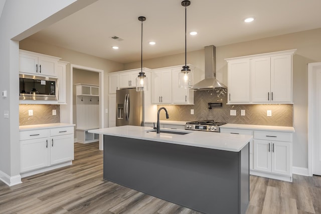 kitchen with light wood finished floors, stainless steel appliances, visible vents, a sink, and wall chimney exhaust hood