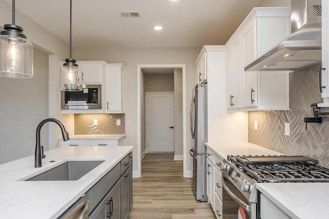 kitchen featuring a sink, visible vents, white cabinets, wall chimney range hood, and appliances with stainless steel finishes