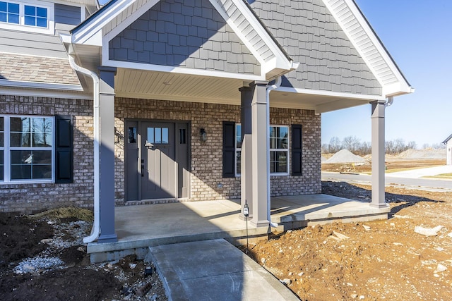 view of exterior entry featuring covered porch and brick siding