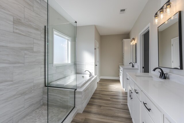 full bath featuring two vanities, a sink, baseboards, and wood finished floors