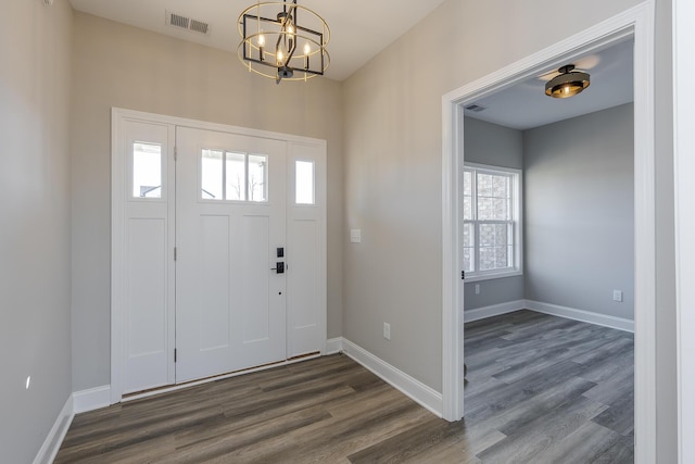 foyer entrance with dark wood-type flooring, a chandelier, visible vents, and baseboards