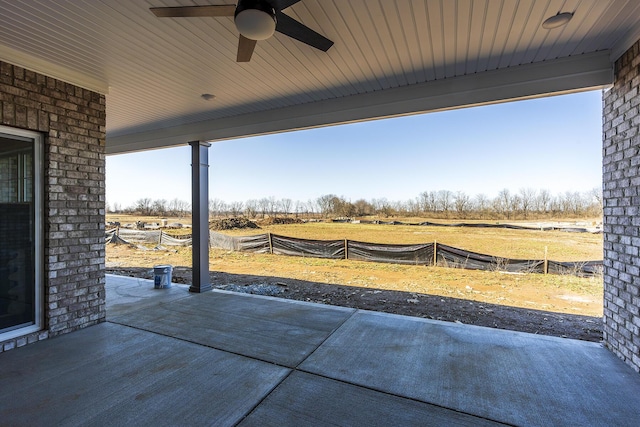 view of patio with a rural view, fence, and a ceiling fan