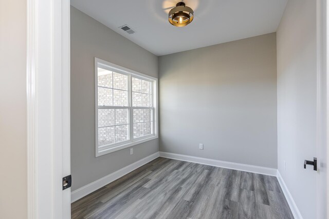 empty room with a notable chandelier, dark wood-type flooring, visible vents, and baseboards