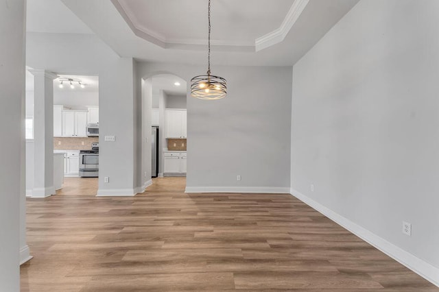 unfurnished dining area with ornamental molding, a tray ceiling, and light hardwood / wood-style flooring