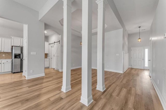 interior space with a barn door, decorative columns, and light hardwood / wood-style flooring