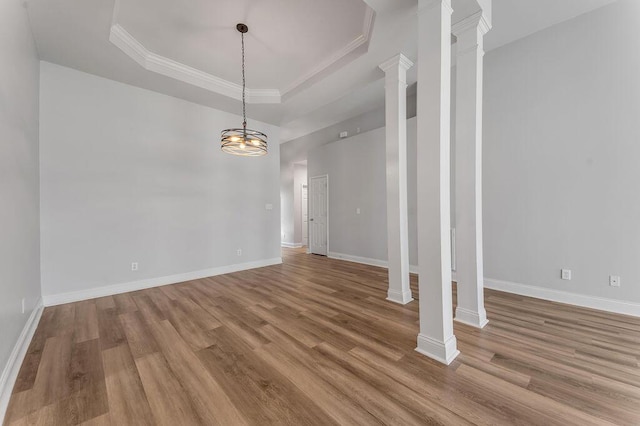 interior space featuring a tray ceiling, ornamental molding, decorative columns, and light hardwood / wood-style floors