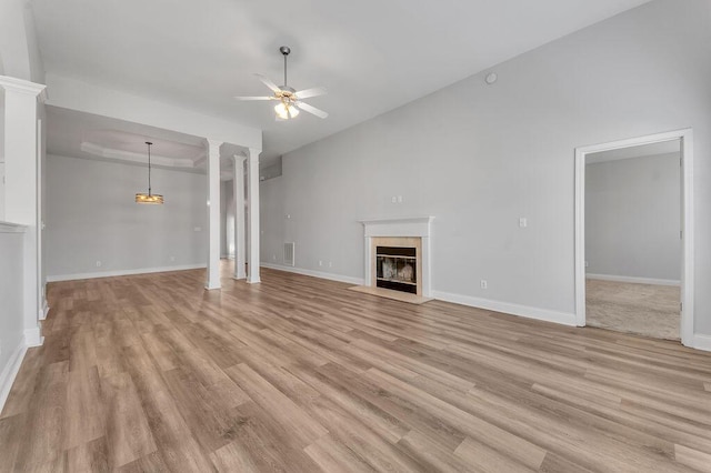 unfurnished living room featuring ceiling fan, a tiled fireplace, light wood-type flooring, and ornate columns