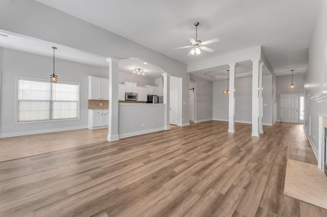 unfurnished living room featuring ornate columns, ceiling fan, and light wood-type flooring