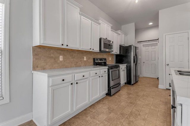 kitchen with backsplash, appliances with stainless steel finishes, a barn door, and white cabinets