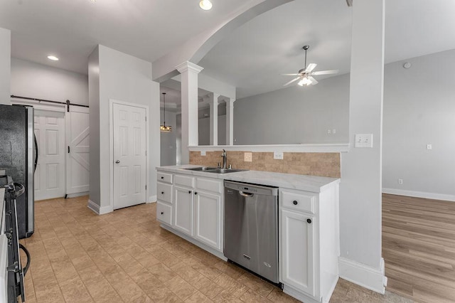 kitchen with ceiling fan, stainless steel appliances, a barn door, decorative columns, and white cabinets