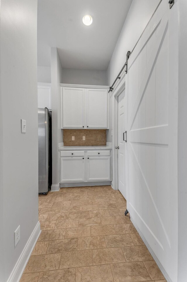 interior space featuring stainless steel refrigerator, white cabinetry, a barn door, and decorative backsplash