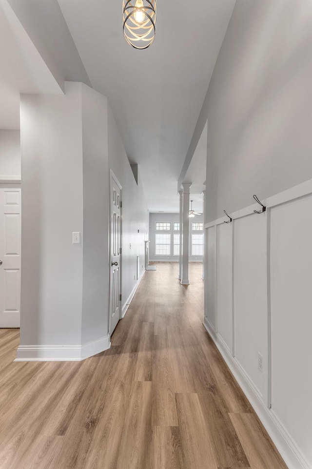 corridor with light hardwood / wood-style floors and decorative columns