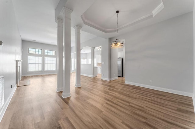 unfurnished living room featuring a tray ceiling, light hardwood / wood-style flooring, ornamental molding, and ornate columns