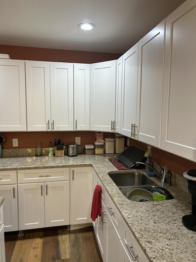 kitchen featuring sink, light stone countertops, dark hardwood / wood-style floors, and white cabinets