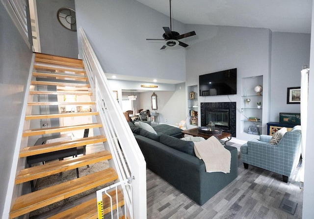 living room featuring ceiling fan, high vaulted ceiling, hardwood / wood-style floors, and a tile fireplace