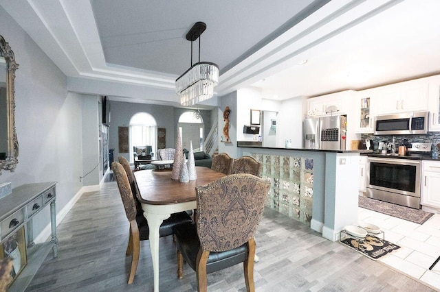 dining room with an inviting chandelier, a tray ceiling, and light hardwood / wood-style flooring