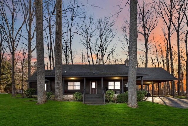 back house at dusk with a carport and a yard