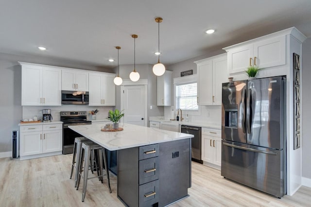 kitchen featuring decorative backsplash, light wood-style flooring, a center island, stainless steel appliances, and white cabinetry