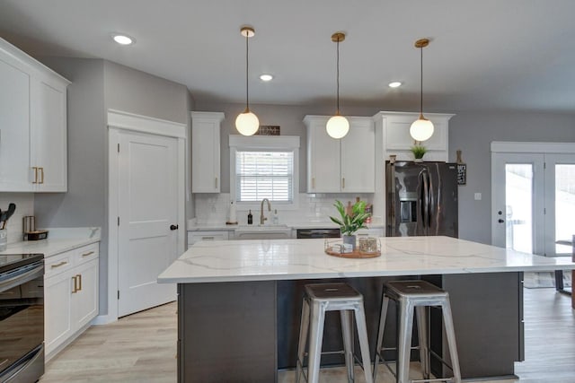 kitchen featuring stainless steel fridge, white cabinets, backsplash, black electric range oven, and a sink