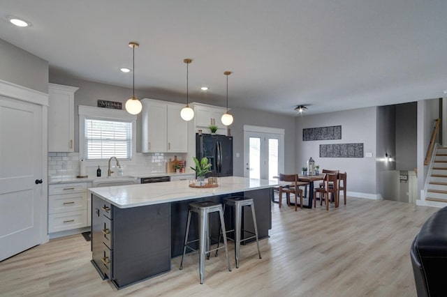 kitchen with a sink, a kitchen island, white cabinetry, french doors, and black fridge