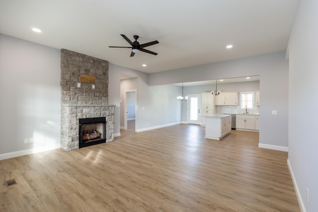 unfurnished living room with ceiling fan with notable chandelier, sink, a fireplace, and light hardwood / wood-style floors