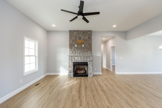 unfurnished living room with ceiling fan, a stone fireplace, and light wood-type flooring