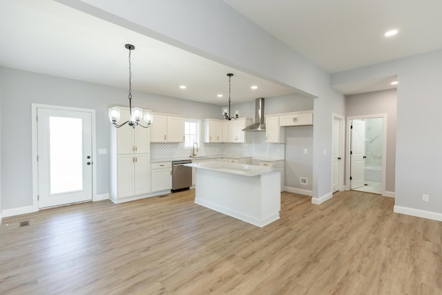 kitchen with white cabinetry, hanging light fixtures, dishwasher, a kitchen island, and wall chimney range hood