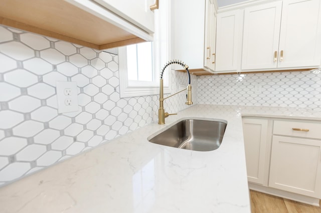 kitchen featuring light stone counters, sink, decorative backsplash, and white cabinets