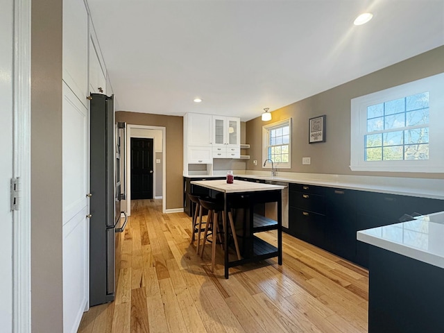 kitchen with dishwashing machine, a breakfast bar, light wood-type flooring, white cabinets, and stainless steel refrigerator