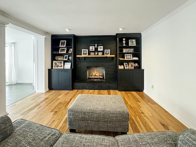 living room featuring a fireplace, ornamental molding, built in shelves, and wood-type flooring