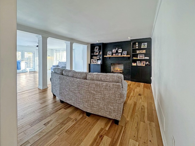 living room featuring decorative columns, built in shelves, a fireplace, and wood-type flooring