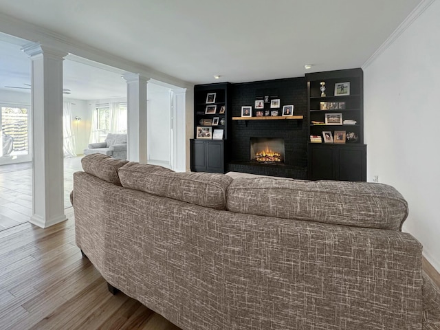 living room featuring hardwood / wood-style flooring, crown molding, a fireplace, ornate columns, and built in features