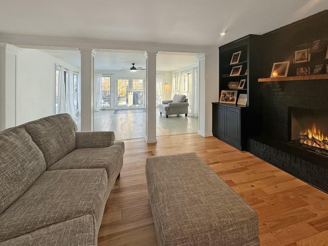 living room with a fireplace, light hardwood / wood-style flooring, decorative columns, and ceiling fan