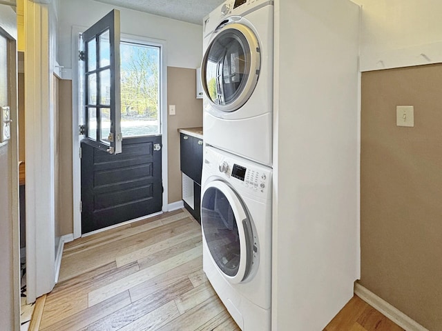 laundry room with light hardwood / wood-style floors and stacked washing maching and dryer