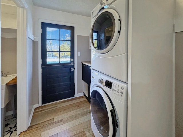 laundry room with stacked washing maching and dryer and light hardwood / wood-style flooring