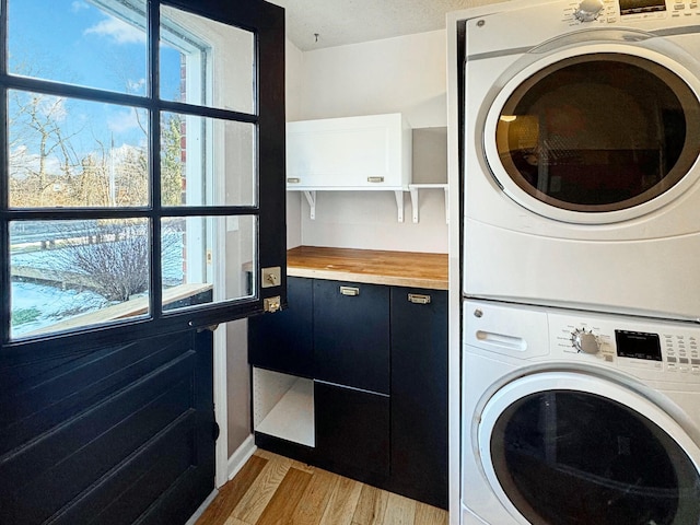 laundry area with light hardwood / wood-style floors, stacked washer / drying machine, and a wealth of natural light