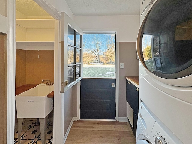 entryway featuring light wood-type flooring, stacked washer and clothes dryer, a textured ceiling, and sink