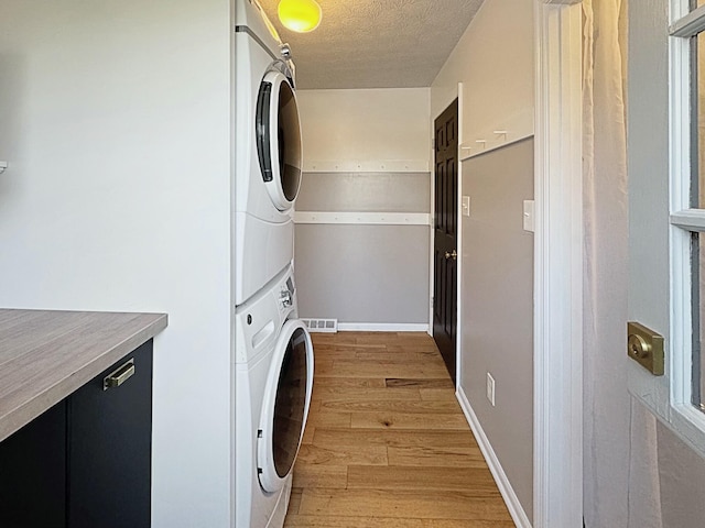 laundry area with a textured ceiling, stacked washer / dryer, and light hardwood / wood-style floors