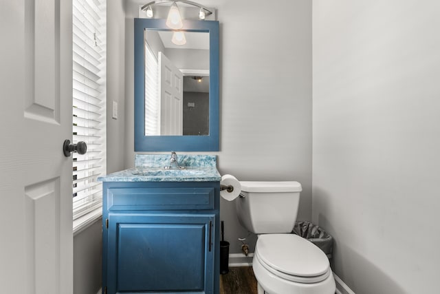 half bath with toilet, baseboards, wood finished floors, and vanity