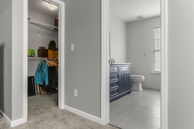 bathroom with a walk in closet, vanity, toilet, and visible vents