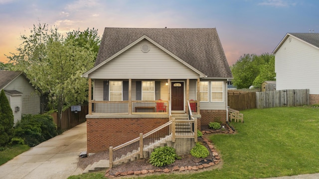 view of front facade with fence, covered porch, a shingled roof, and a yard