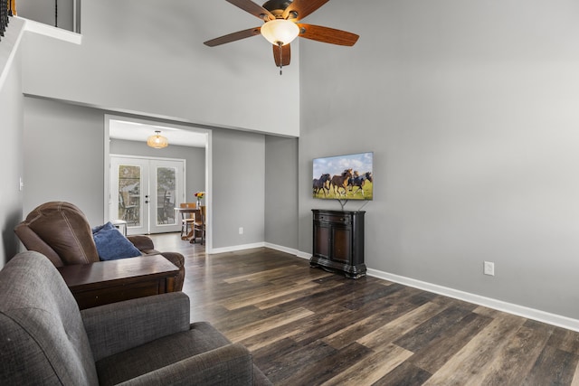 living area with french doors, a ceiling fan, baseboards, wood finished floors, and a towering ceiling