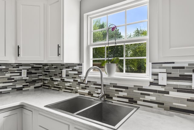 kitchen with light countertops, white cabinetry, a sink, and backsplash